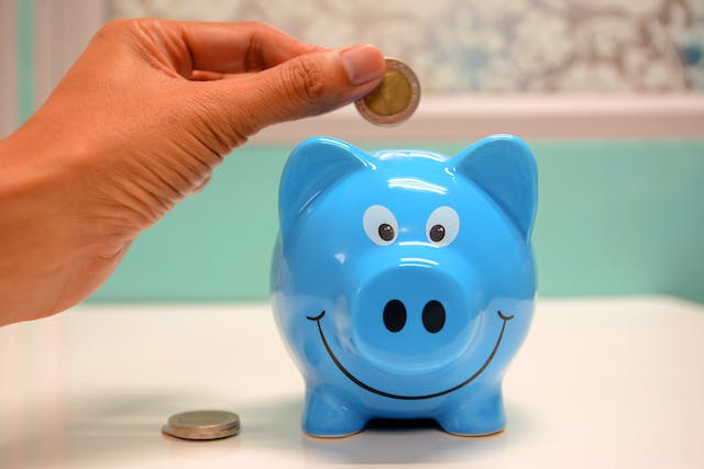 Stock photo of a hand dropping coins into a smiling piggy bank.